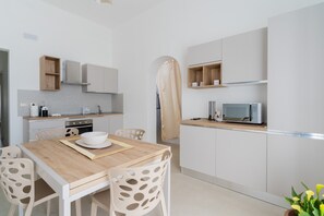 Uma cozinha moderna com armários brancos, uma mesa de jantar de madeira e um micro-ondas.
