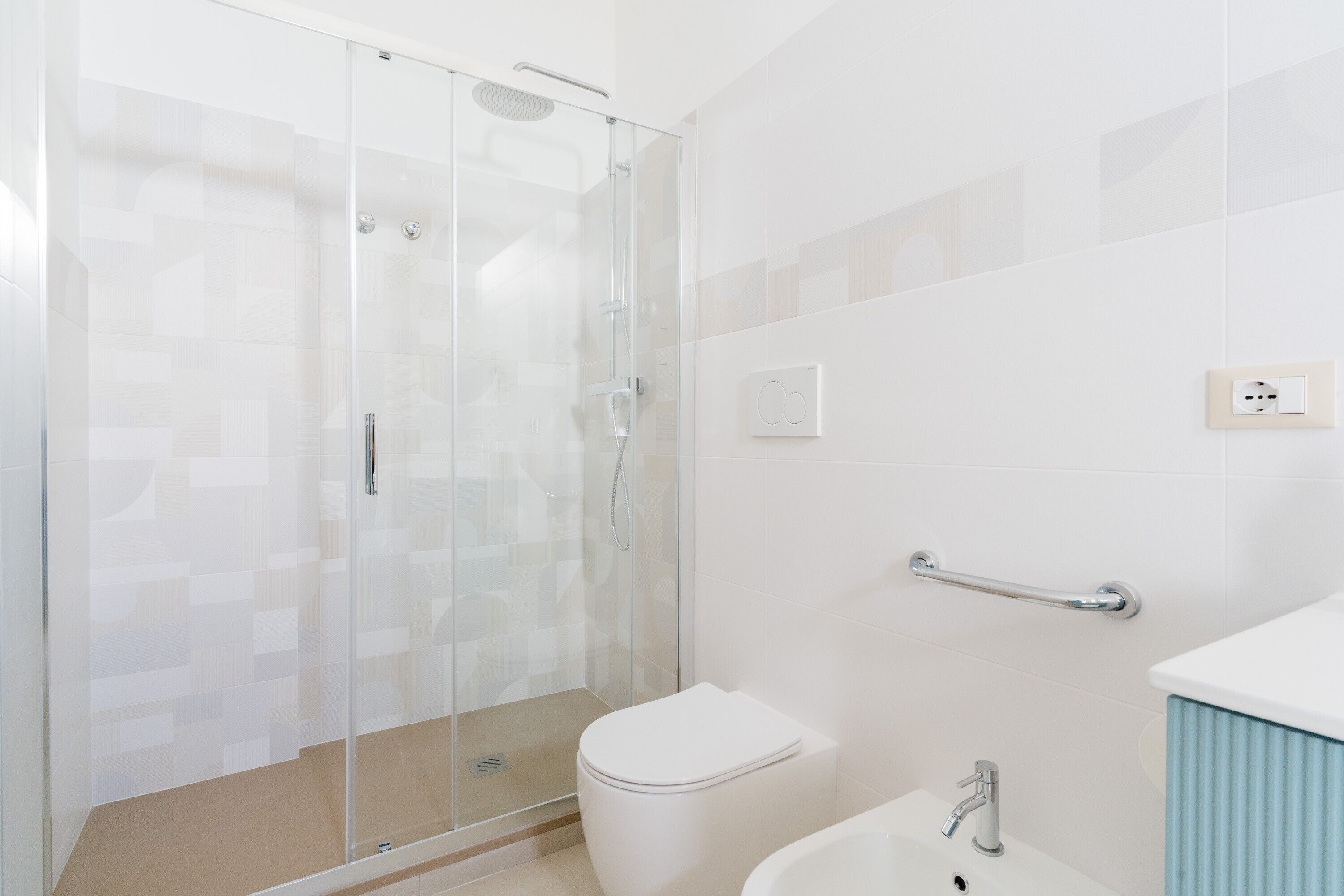 Ein modernes Badezimmer mit Duschkabine aus Glas, einer weißen Toilette, einem Waschbecken mit Armatur und einem Handtuchhalter.