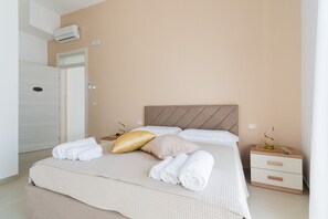 Una cama bien hecha con toallas enrolladas, una mesita de noche con lámpara y un equipo de aire acondicionado en la pared.