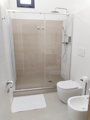 Un bany modern amb dutxa de vidre, vàter i bidet.