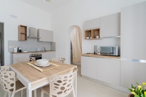 A modern kitchen with white cabinetry, a wooden dining table, and a microwave. - Bed and Breakfast 'Camera Jacky' with Balcony, Wi-Fi and Air Conditioning (Galatone)