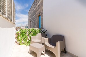 A balcony with two chairs and a small table, a lattice fence with greenery, and a building with a blue door. - Bed and Breakfast 'Camera Jacky' with Balcony, Wi-Fi and Air Conditioning (Galatone)