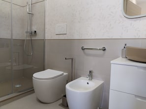A modern bathroom with a glass-enclosed shower, a toilet, a bidet, and a sink with a mirror above.