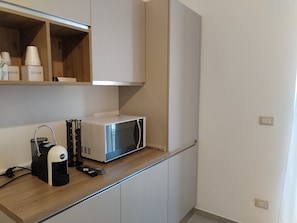 A kitchen with a microwave, a coffee machine, and sugar and coffee cups on the shelf.