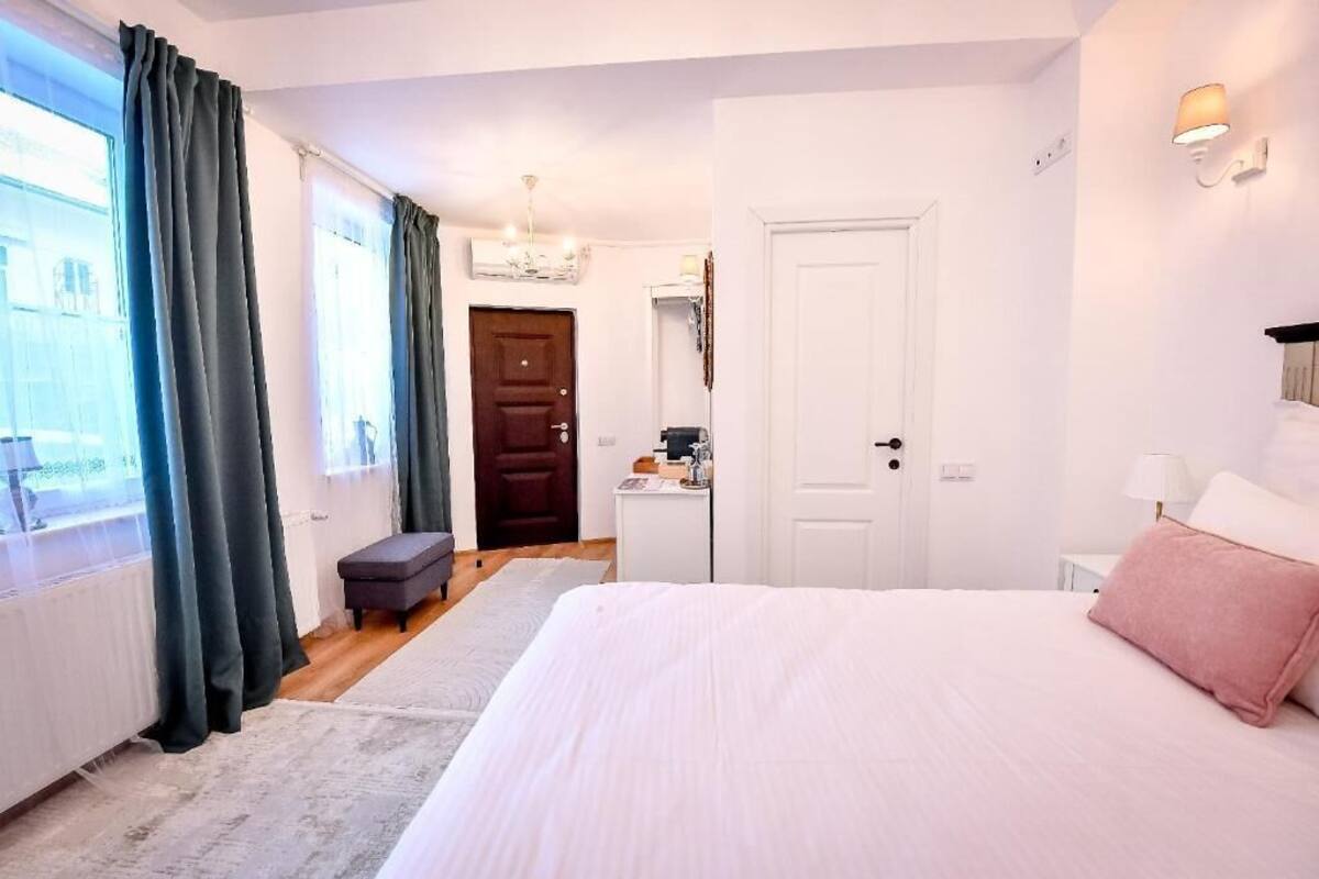 A bedroom with a bed, a desk, a chair, a door, and a window with curtains.