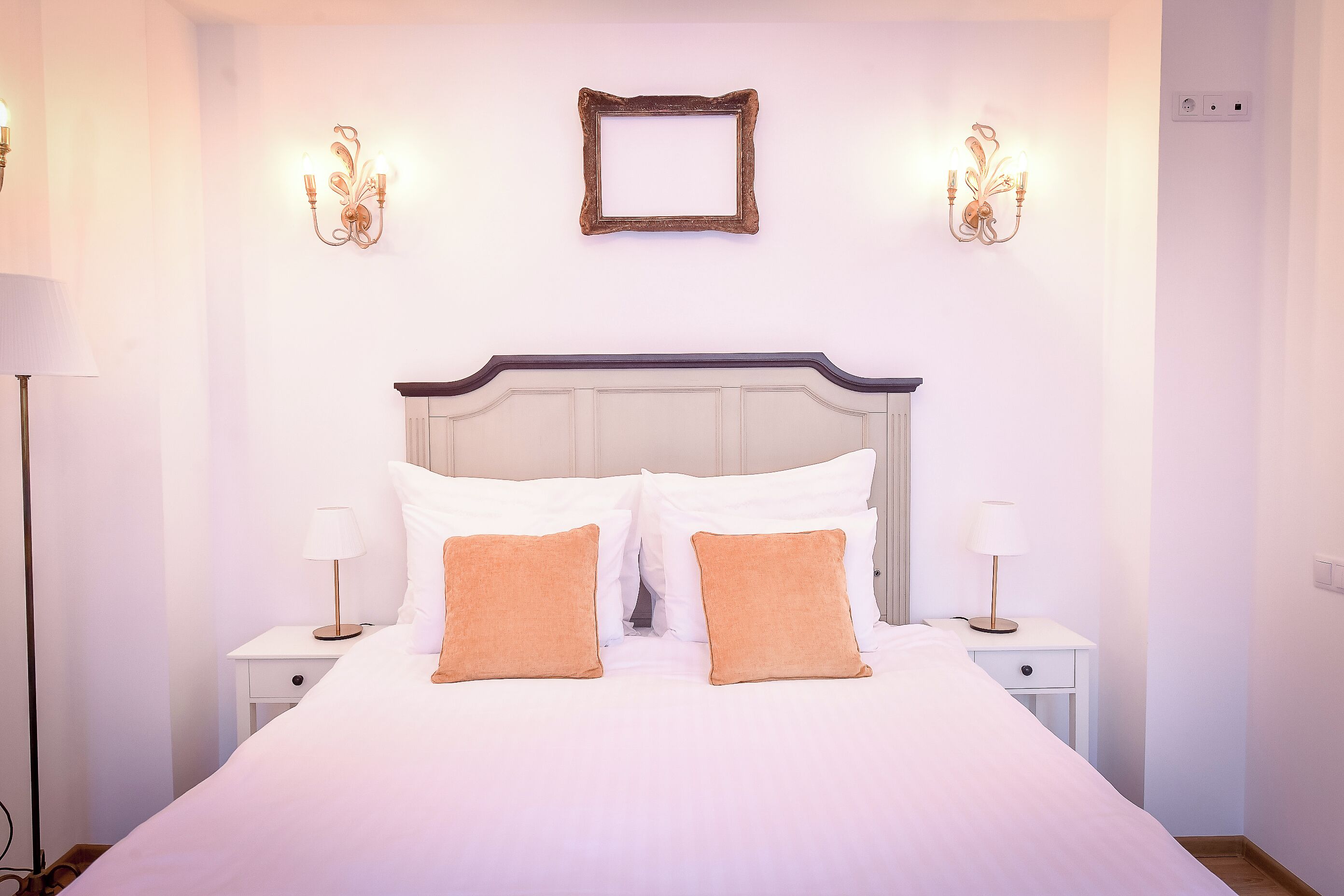 A neatly made bed with two pillows, a bedside table with a lamp, and wall sconces.