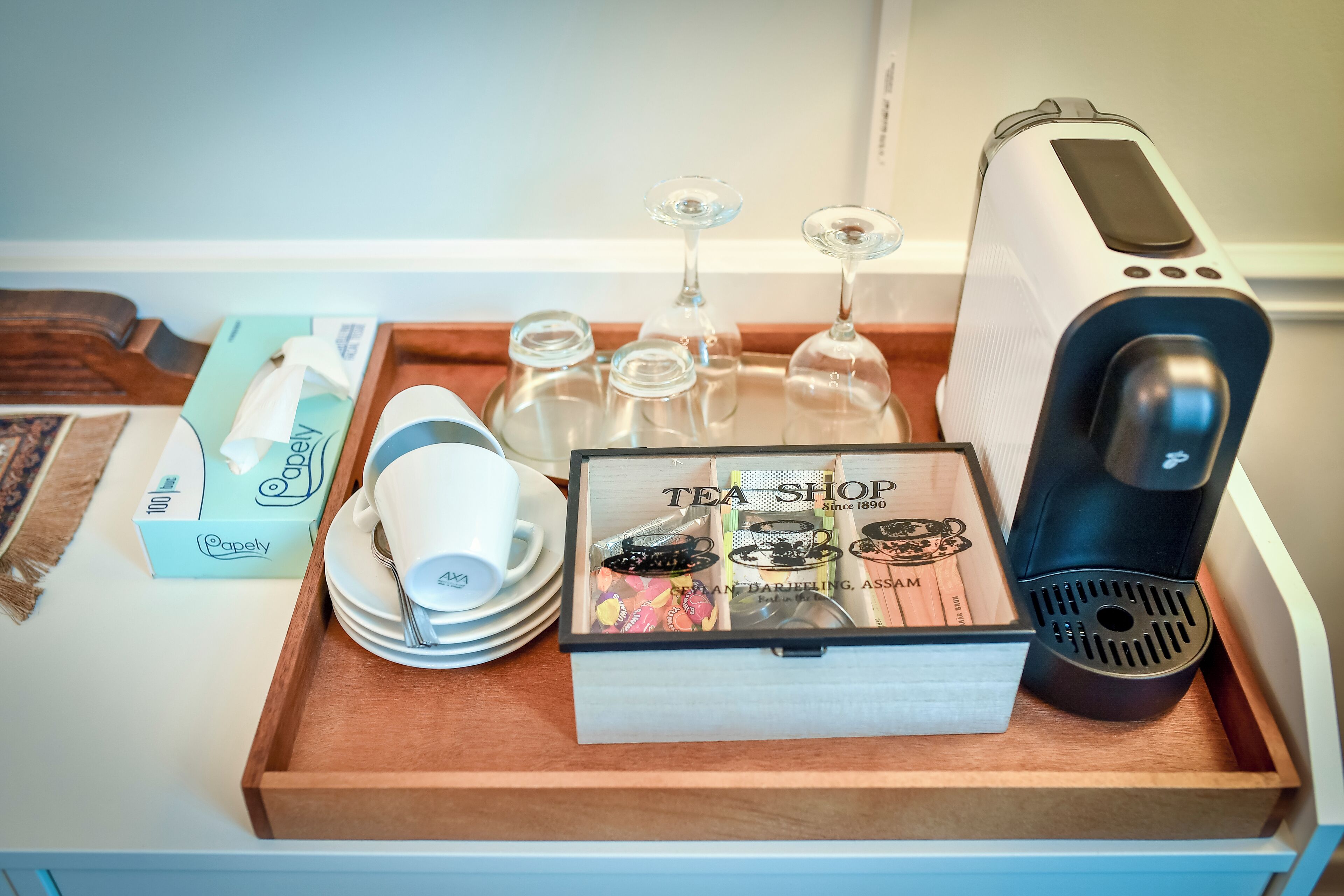A tray with a tea shop box, a coffee maker, and glassware on a wooden surface.