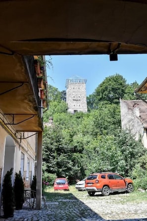 Mukulakivipolku johtaa historialliseen torniin. Lähellä on parkissa punainen auto, ja polun vasemmalla puolella on katettu alue.
