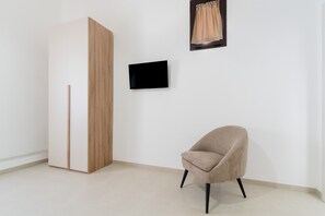A room with a wardrobe, a chair, a flat-screen TV, and a framed picture on the wall.