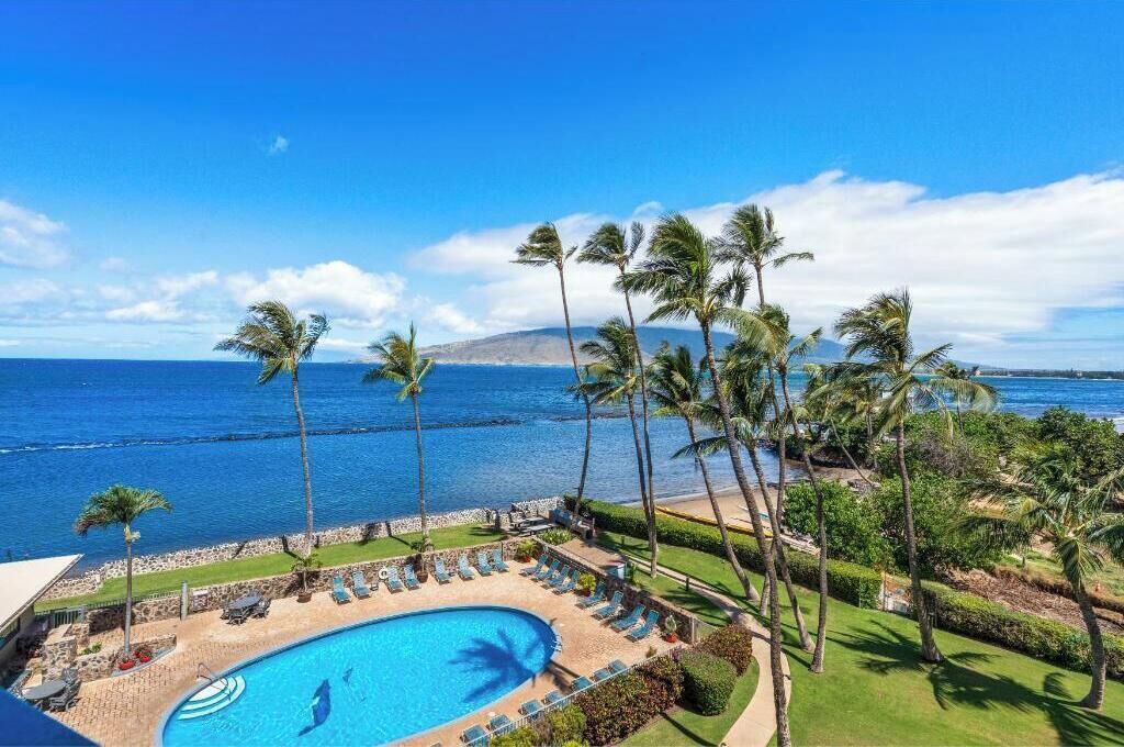 A pool area with lounge chairs and palm trees, overlooking a body of water.