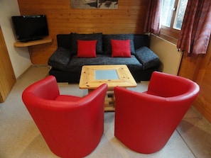 A room with a sofa, two red chairs, a wooden coffee table, and a television on a stand. - 3-room apartment for 4 persons : Living room - kitchen with dishwasher and filtercoffeemachine- 1 ro (Grimentz)