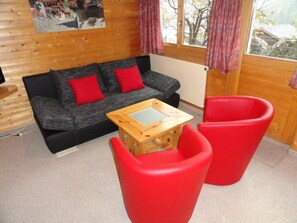 A room with a sofa, two red chairs, a wooden table, and a window with curtains. - 3-room apartment for 4 persons : Living room - kitchen with dishwasher and filtercoffeemachine- 1 ro (Grimentz)