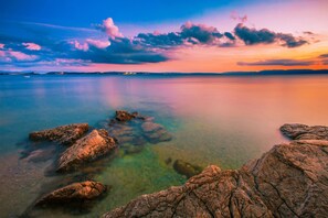 Una masa de agua tranquila con rocas visibles al frente y una costa lejana.
