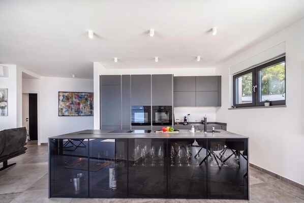 A modern kitchen with a central island, built-in appliances, and a large window. - Pool Villa Solea /w Panoramic Sea View (Kostrena)