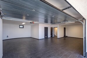 Un grand garage spacieux et vide, avec un plafond haut, des carreaux de sol sombres et un aménagement épuré et minimaliste.