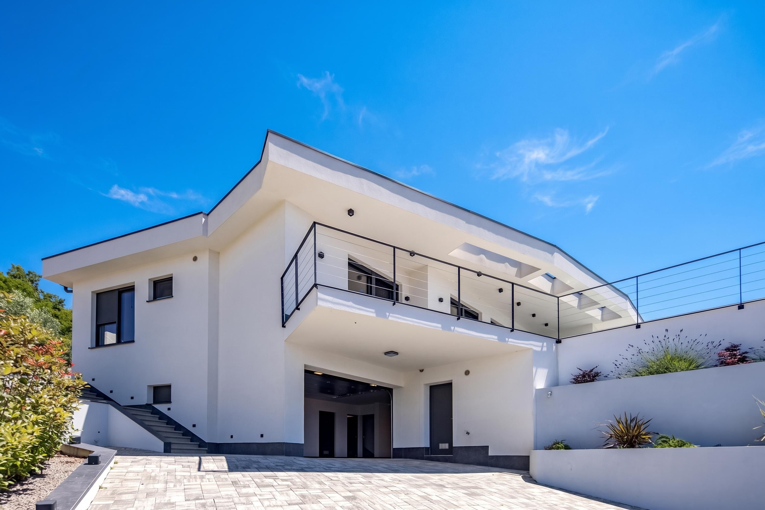 A modern two-story house with a flat roof, large windows, and a balcony.