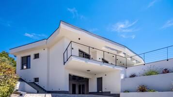 A modern two-story house with a flat roof, large windows, and a balcony.