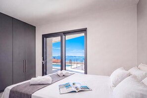 A modern hotel room with a large bed, a view of the sea, and a balcony with a pool. - Pool Villa Solea /w Panoramic Sea View (Kostrena)