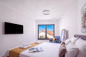 A hotel room with a bed, a flat-screen TV, a window with a view of buildings, a chair, and a framed picture. - Pool Villa Solea /w Panoramic Sea View (Kostrena)