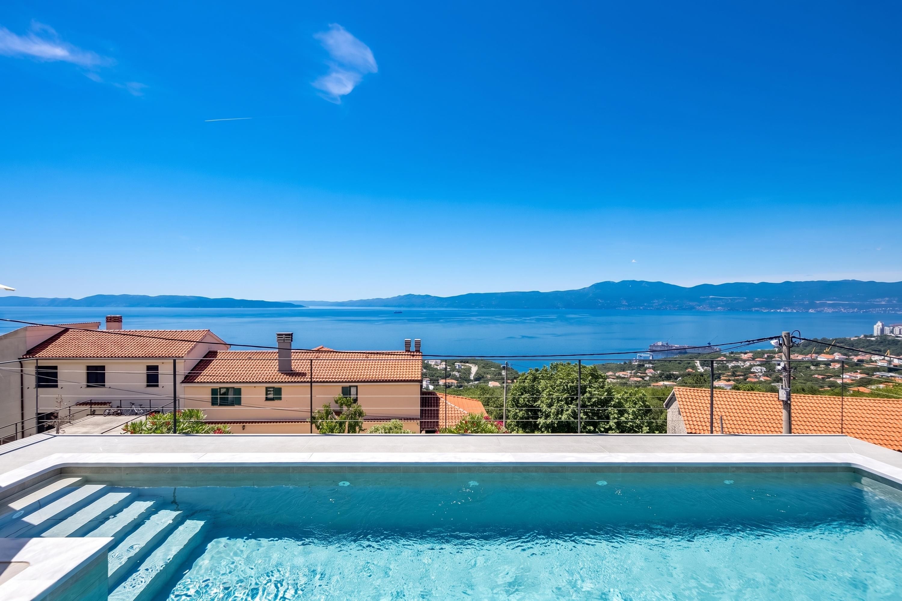 A swimming pool with a view of the sea and distant mountains.