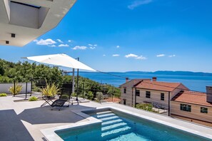 Un espace piscine avec vue sur la mer, un parasol blanc et une chaise.