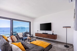 A modern living room with a large window, a flat-screen TV, a sofa, and a coffee table. - Pool Villa Solea /w Panoramic Sea View (Kostrena)