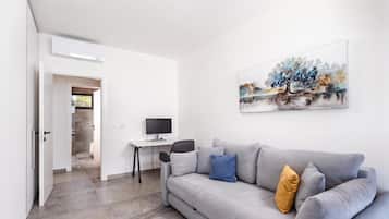 A modern living room with a grey sofa, a desk with a computer, and a painting on the wall.