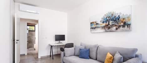 A modern living room with a grey sofa, a desk with a computer, and a painting on the wall.