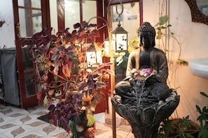 A Buddha statue, a water feature, and a potted plant with hanging lights. - Ayuskama Ayurveda Ayur Yoga (Rishikesh)
