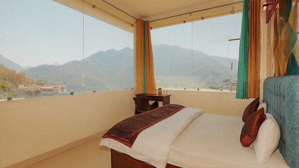 A bedroom with a bed, a view of mountains, and a balcony. - Ayuskama Ayurveda Ayur Yoga (Rishikesh)