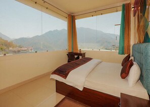 A bedroom with a bed, a view of mountains, and a balcony. - Ayuskama Ayurveda Ayur Yoga (Rishikesh)