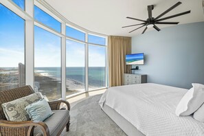 A bedroom with a large window, a bed, a TV, and a ceiling fan. - Turquoise Place 2401C by Liquid Life (Orange Beach)