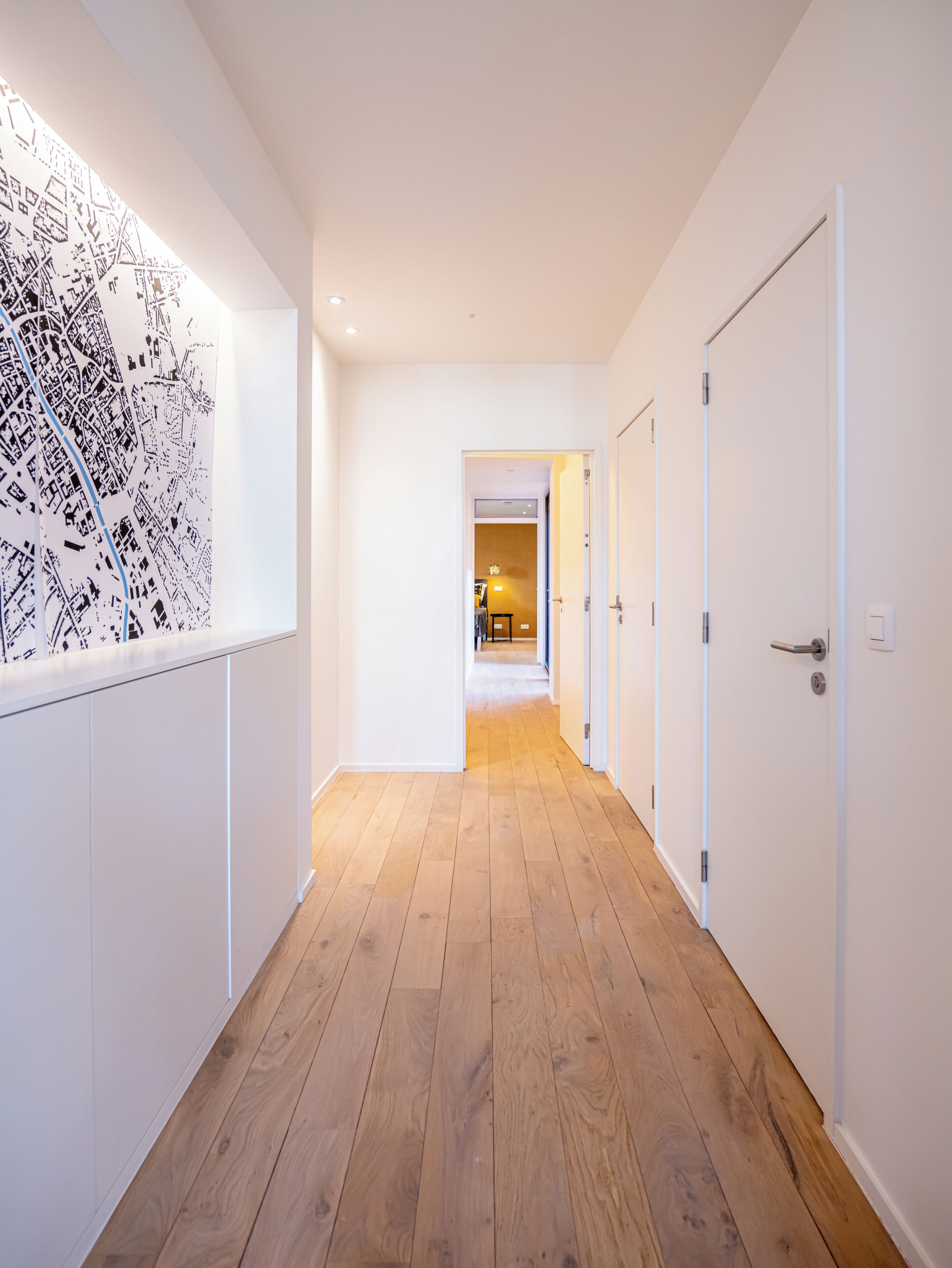 A hallway with wooden flooring, white walls, and a door at the end.