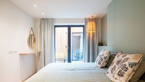 A bedroom with a bed, a bedside table, a mirror, a window with curtains, and a view of the outside.