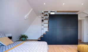 Une chambre à coucher moderne avec un lit, une table de chevet, une plante en pot et un escalier avec un mur sombre et des marches en bois.