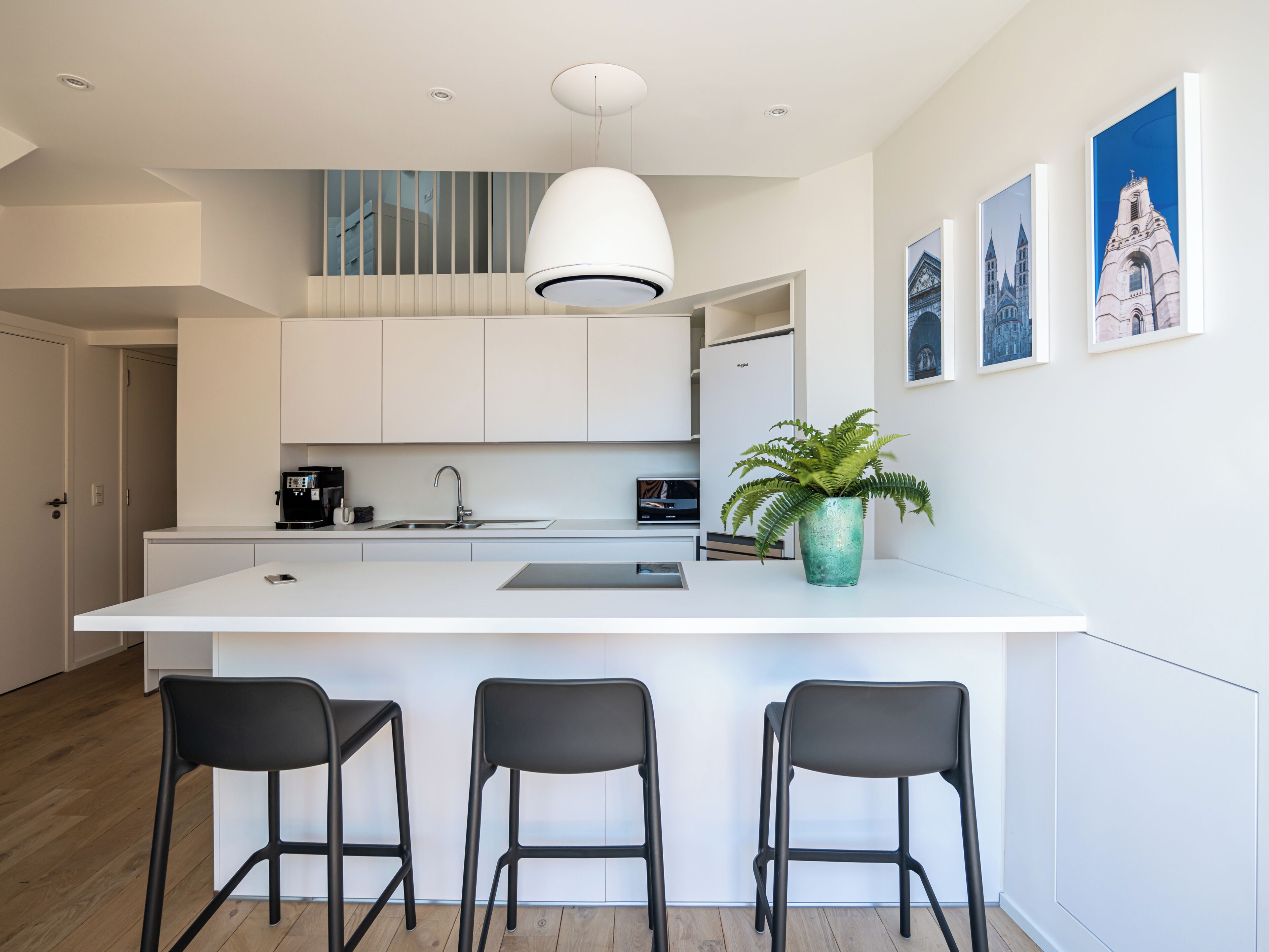 A modern kitchen with a central island, bar stools, a coffee machine, and a potted plant.