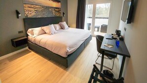Moderni hotellihuone, jossa on sänky, työpöytä, tuoli, taulutelevisio ja suuri ikkuna.