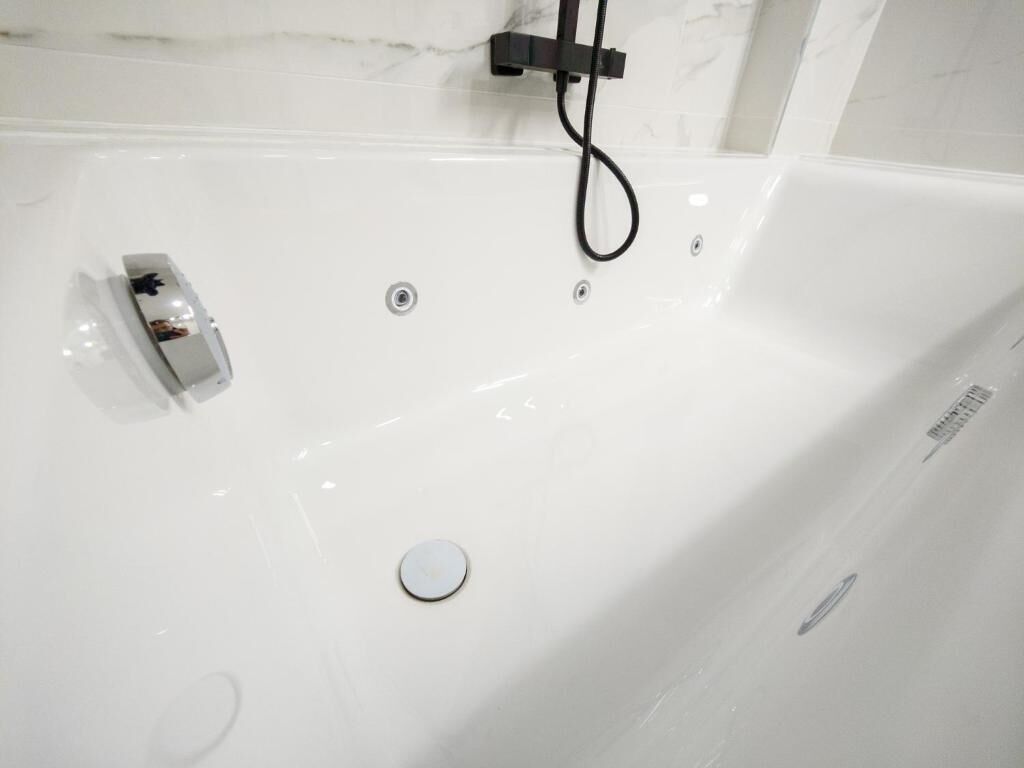 A white bathtub with a handheld showerhead, a control panel, and a drain.