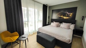 Moderni hotellihuone, jossa on suuri sänky, sohva, pieni pöytä ja taulu seinällä.