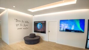 Un interior moderno con un sofá curvo, una pared con una cita motivacional, un cartel enmarcado y una gran pantalla de televisión que muestra una escena natural.
