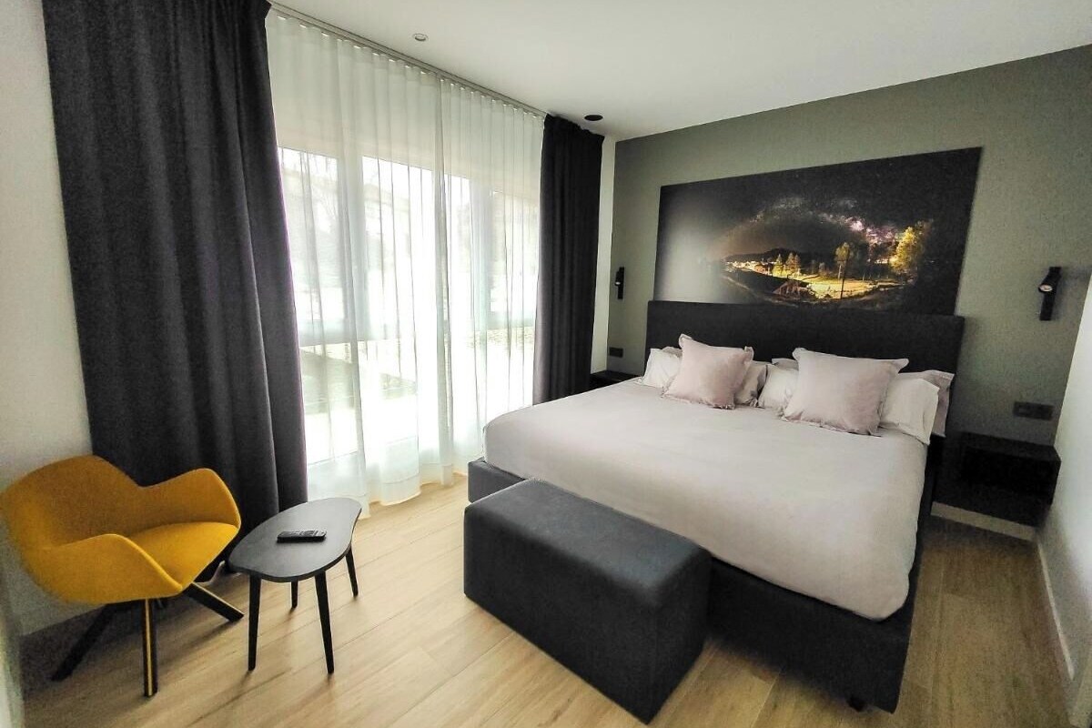 Moderni hotellihuone, jossa on suuri sänky, pieni sohva, sohvapöytä ja taulu seinällä.