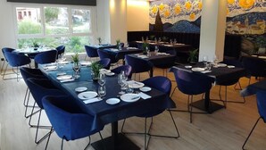 Un restaurante con varias mesas, sillas azules y un ventanal grande.