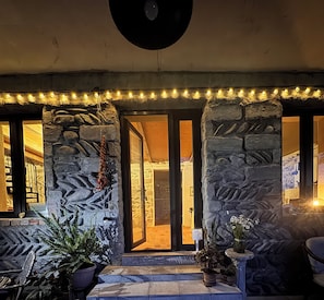 A stone facade with a doorway, potted plants, and string lights.