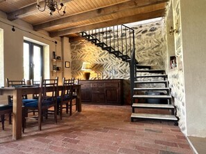 Un comedor con piso de ladrillo, mobiliario de madera, una escalera con paredes de piedra y un candelabro.