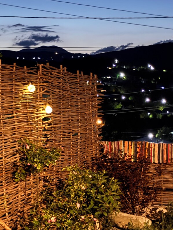 Un entorno rústico al aire libre con una estructura tejida, luces colgantes y montañas al fondo.