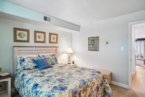 Ein Schlafzimmer mit einer blumigen Bettdecke, einem hölzernen Kopfteil, Nachttischen, einer Lampe und gerahmten Bildern an der Wand.