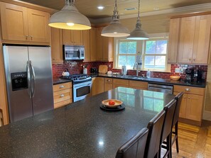 Una cocina con armarios de madera, electrodomésticos de acero inoxidable, encimera de granito e iluminación colgante.