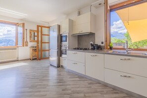 Eine moderne Küche mit weißen Schränken, Edelstahlgeräten und einem großen Fenster mit Blick ins Freie.