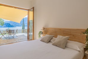 Une chambre à coucher avec un grand lit, une tête de lit en bois et une vue sur un lac, visible à travers une porte vitrée.