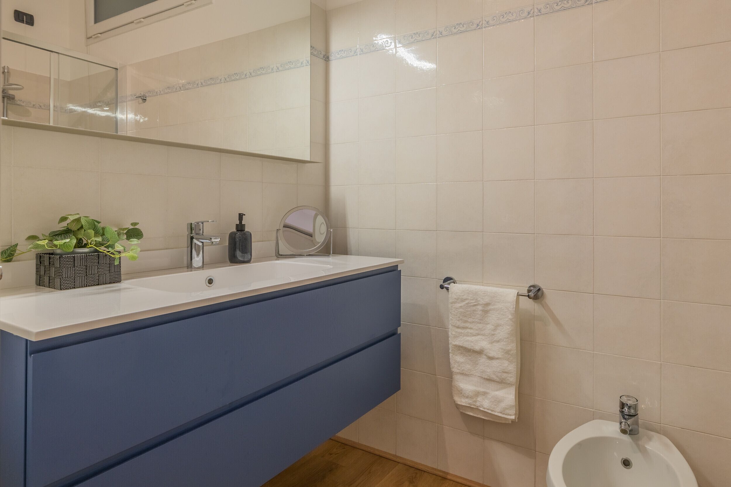 A bathroom with a white sink, blue cabinet, mirror, and a white towel hanging on the wall.